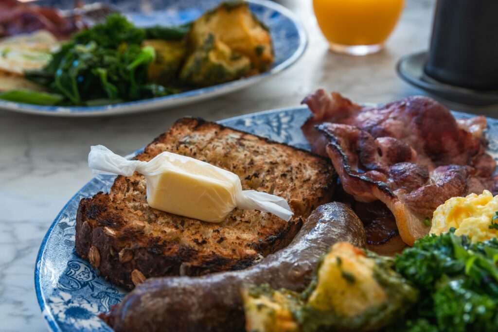 A hearty English breakfast featuring bacon, eggs, sausage, bread, and fresh greens.