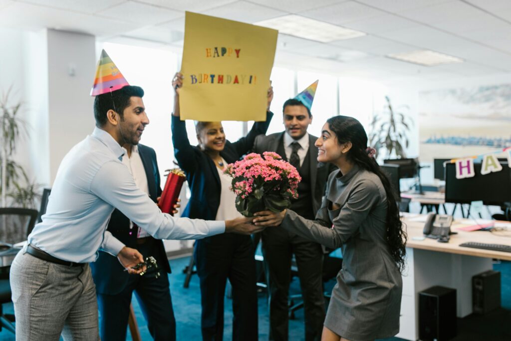 Happy office birthday celebration with colleagues exchanging gifts and wearing party hats.